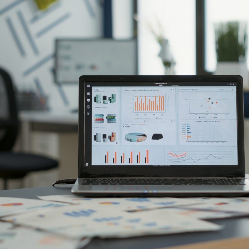 Closeup of laptop screen with enterprise resource planning showing moving charts and growing turnover in empty startup office. Interior of sales department with portable computer with erp software.